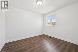 Room featuring wood-finish flooring, white baseboards, a single window with white trim, and a flush-mount ceiling light fixture - 