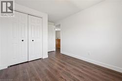 Interior room featuring wood-finish flooring, white walls, and white bi-fold closet doors with black hardware - 