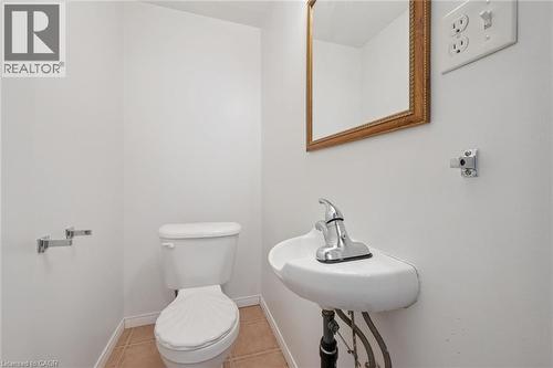 Compact powder room featuring a wall-mounted sink with chrome faucet, a standard toilet, and neutral-toned floor tiling - 71 Peach Blossom Crescent, Kitchener, ON 