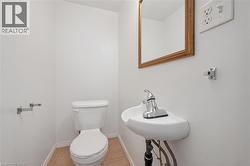 Compact powder room featuring a wall-mounted sink with chrome faucet, a standard toilet, and neutral-toned floor tiling - 