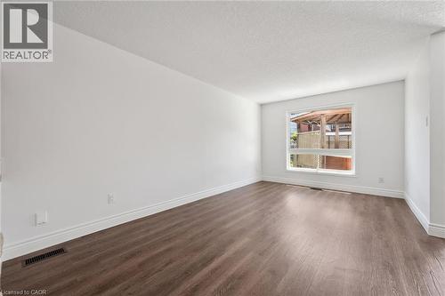 Spacious room featuring wood-finish flooring, white baseboards, and a large window with white trim - 71 Peach Blossom Crescent, Kitchener, ON 