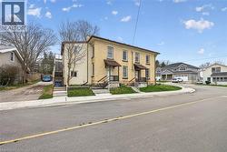 Two-story brick and siding structure featuring two separate entrances, individual front porches, an exterior staircase, and a gravel driveway - 