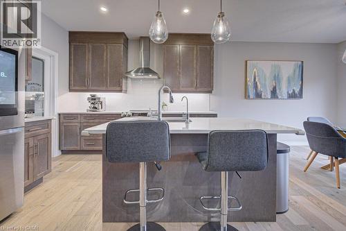 Kitchen featuring an expansive island with a light-toned countertop, wood-finish cabinetry, stainless steel appliances, and wood-finish flooring - 15 Matheson Crescent, Innerkip, ON - Indoor