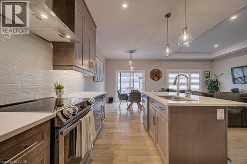 Gourmet kitchen featuring wood-finish cabinetry, light-toned countertops, a subway tile backsplash, stainless steel appliances, and an island with an integrated sink - 15 Matheson Crescent, Innerkip, ON - Indoor Photo Showing Kitchen With Double Sink With Upgraded Kitchen
