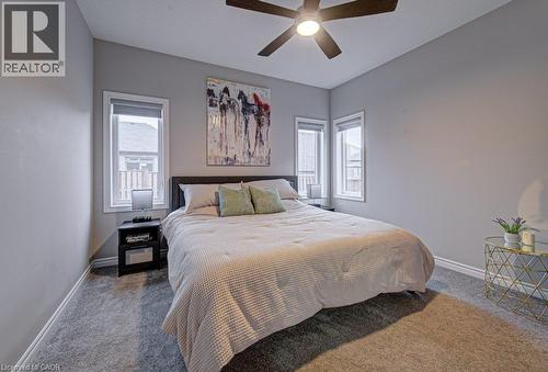 Carpeted room featuring light gray walls, a ceiling fan with integrated lighting, and two windows with white trim - 15 Matheson Crescent, Innerkip, ON - Indoor Photo Showing Bedroom