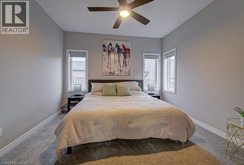 Carpeted bedroom featuring a dark-finish ceiling fan with light, light gray walls, white baseboards, and two windows with white trim - 15 Matheson Crescent, Innerkip, ON - Indoor Photo Showing Bedroom