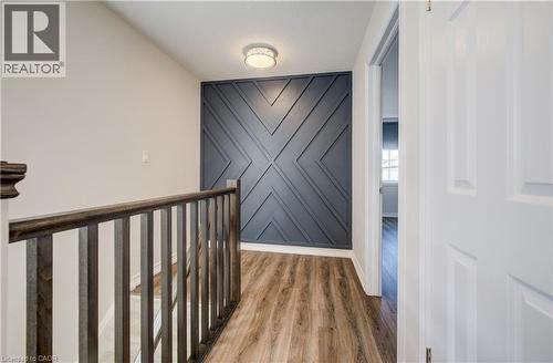 Upper-level hallway featuring wood-finish flooring, a decorative accent wall with geometric paneling, and a contemporary flush-mount ceiling light - 80 Miranda Path, Elmira, ON - Indoor Photo Showing Other Room