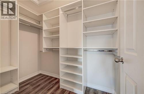 Walk-in closet featuring custom white built-in shelving, multiple hanging rods, and wood-finish flooring - 80 Miranda Path, Elmira, ON - Indoor With Storage