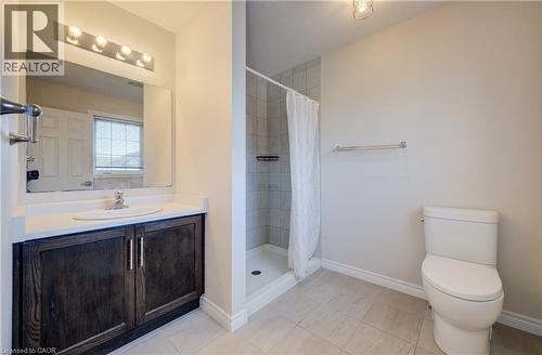 Bathroom featuring a dark wood-finish vanity with a white countertop and integrated sink, a tiled shower enclosure, a standard toilet, and neutral-toned floor tiling - 80 Miranda Path, Elmira, ON - Indoor Photo Showing Bathroom