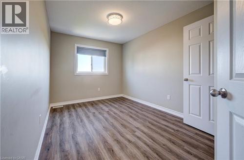Wood-finish flooring throughout, featuring a window with a roller shade, a ceiling-mounted light fixture, and white painted trim - 80 Miranda Path, Elmira, ON - Indoor Photo Showing Other Room