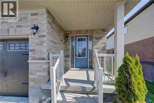 Brick and stone facade featuring a covered front porch with white railings, a blue entry door with a sidelight, and a decorative outdoor light fixture - 80 Miranda Path, Elmira, ON - Outdoor With Exterior