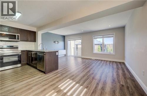 Open-concept living area featuring wood-finish flooring, a kitchen island with a sink and stainless steel appliances, recessed lighting, and sliding glass doors to the exterior - 80 Miranda Path, Elmira, ON - Indoor Photo Showing Kitchen