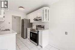 Kitchen featuring white cabinetry, stainless steel appliances, a double basin sink, white countertops, and a textured white backsplash - 
