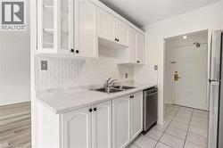 Bright kitchen featuring white cabinetry with black hardware, a stainless steel sink, and a white patterned backsplash - 