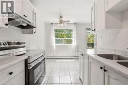 Kitchen featuring white cabinetry with black hardware, stainless steel appliances, a double basin sink, and white tiled flooring - 