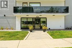Entryway featuring a glass-paneled door, upper-level balcony with a glass railing, white exterior walls, and a concrete pathway - 
