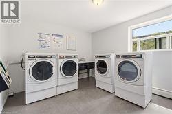 Dedicated laundry facility featuring multiple commercial-grade washers and dryers, a utility sink, durable tile flooring, and ample natural light from a large window - 