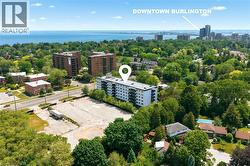 Aerial perspective showcasing the residential building with multiple balconies, surrounded by mature trees, a clear body of water, and distant city structures - 