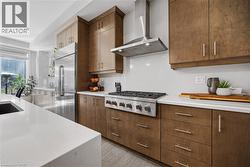 Kitchen with wall chimney range hood, stainless steel appliances, and light stone counters - 