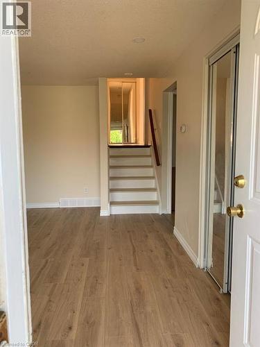 Entryway featuring wood-finish flooring, light neutral wall paint, white baseboards, and a staircase with a dark wood handrail - 86 Belwood Crescent, Kitchener, ON - Indoor Photo Showing Other Room