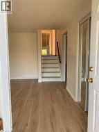 Entryway featuring wood-finish flooring, light neutral wall paint, white baseboards, and a staircase with a dark wood handrail - 