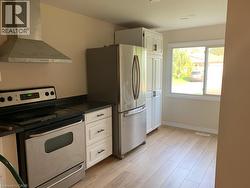 Modern kitchen featuring wood-finish flooring, white cabinetry, stainless steel appliances, a range hood, and a large window - 