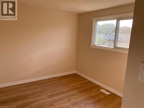 Bright interior room featuring a large window with white trim, wood-finish flooring, neutral wall tones, and white baseboards - 86 Belwood Crescent, Kitchener, ON - Indoor Photo Showing Other Room
