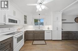 Modern kitchen featuring two-tone cabinetry, white appliances, and wood-finish flooring - 