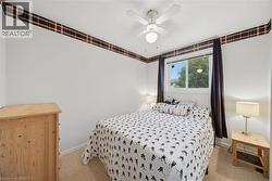 Bedroom with carpeted flooring, a white ceiling fan with integrated lighting, and a window with dark curtain panels - 
