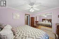 Bedroom featuring mirrored closet doors, a ceiling fan with light fixture, wood-finish flooring, and crown molding - 