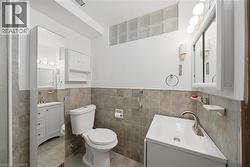 Bathroom featuring a compact white vanity with an integrated sink, a white toilet, and neutral-toned wall tiling - 