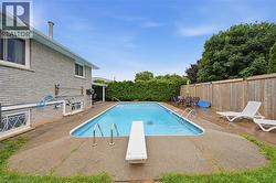 Expansive backyard featuring an in-ground swimming pool with diving board, concrete surround, and a wooden deck - 