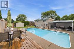 Expansive backyard featuring a rectangular in-ground swimming pool, a wood deck, a concrete patio, and a covered outdoor area - 