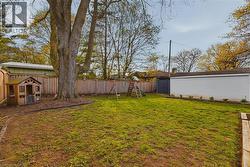 Spacious backyard featuring a large mature tree, wood privacy fencing, a manicured lawn area, and a white siding garage structure with dark gray doors - 