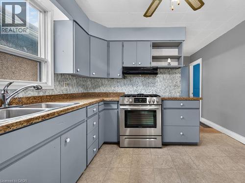 Corner kitchen featuring light blue cabinetry, stone-finish countertops, stainless steel range, a double basin sink, and tile flooring - 23 Harrison Avenue, Hamilton, ON - Indoor Photo Showing Kitchen With Double Sink