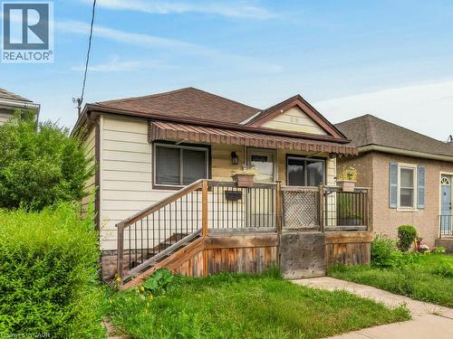 Front exterior featuring siding, a wood porch with black railing, and an entryway awning - 23 Harrison Avenue, Hamilton, ON - Outdoor With Deck Patio Veranda