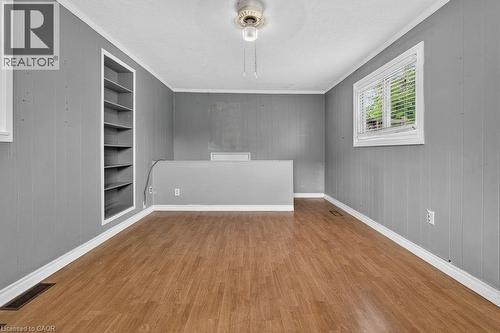 Spacious room featuring wood-finish flooring, light gray vertical paneling, and a built-in shelving unit - 23 Harrison Avenue, Hamilton, ON - Indoor Photo Showing Other Room