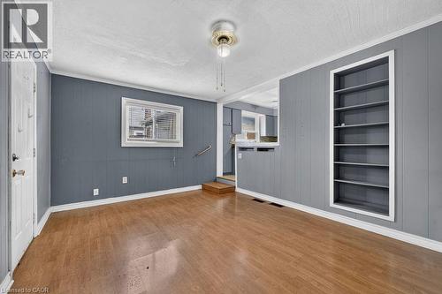 Spacious interior room featuring wood-finish flooring, paneled walls, and a built-in shelving unit - 23 Harrison Avenue, Hamilton, ON - Indoor Photo Showing Other Room