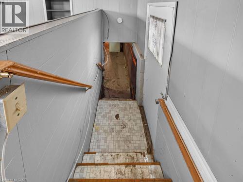 Stairwell featuring light gray paneling, wooden handrails, and a tiled landing - 23 Harrison Avenue, Hamilton, ON - Indoor Photo Showing Other Room