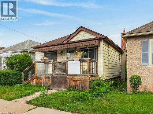 Single-story dwelling with light-colored siding, a brown shingle roof, and a covered front porch featuring a dark awning - 23 Harrison Avenue, Hamilton, ON - Outdoor
