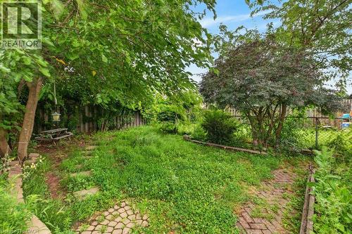 Expansive outdoor space featuring a paved brick pathway, stepping stones, mature trees, and a wooden fence - 23 Harrison Avenue, Hamilton, ON - Outdoor