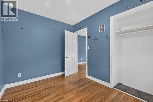Interior room featuring wood-finish flooring, blue walls, white trim, and a white six-panel door - 23 Harrison Avenue, Hamilton, ON - Indoor Photo Showing Other Room