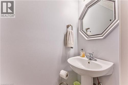 Pedestal sink with chrome faucet, octagonal framed mirror, and a wall-mounted towel ring - 4057 Donnic Drive, Burlington, ON - Indoor Photo Showing Bathroom
