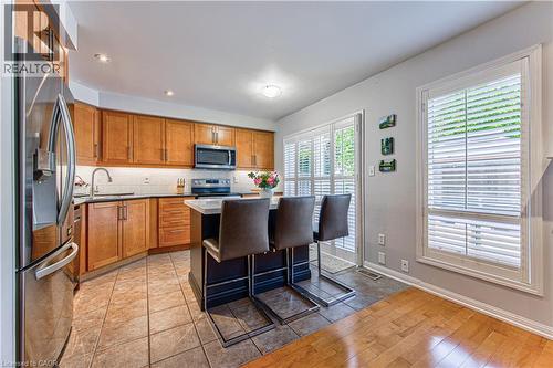 Open-concept kitchen featuring wood cabinetry, stainless steel appliances, a center island with countertop seating, and tile flooring - 4057 Donnic Drive, Burlington, ON - Indoor Photo Showing Kitchen