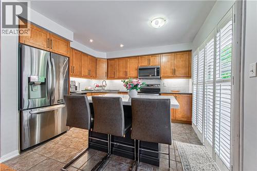 Kitchen featuring wood cabinetry, stainless steel appliances, a center island with seating, a tile backsplash, and white shuttered patio doors - 4057 Donnic Drive, Burlington, ON - Indoor Photo Showing Kitchen