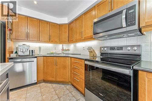 Kitchen featuring wood-finish cabinetry, stainless steel appliances, dark countertops, a tile backsplash, and tile flooring - 4057 Donnic Drive, Burlington, ON - Indoor Photo Showing Kitchen