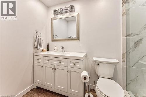 Bathroom featuring a white vanity with integrated sink, a rectangular mirror, a three-light vanity fixture, and wood-finish flooring - 4057 Donnic Drive, Burlington, ON - Indoor Photo Showing Bathroom