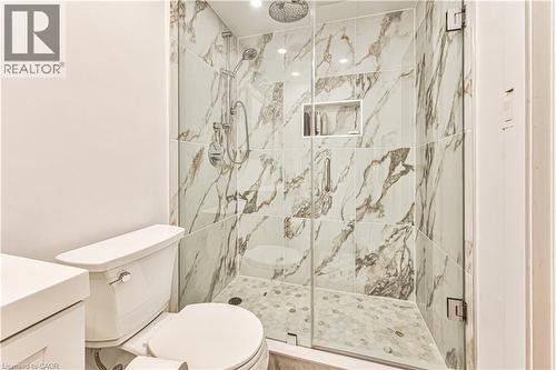 Glass-enclosed shower with large format marble-look tile walls, a pebble-stone floor, and a built-in shower niche - 4057 Donnic Drive, Burlington, ON - Indoor Photo Showing Bathroom