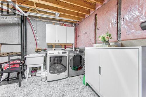 Utility area featuring a laundry sink, two white storage cabinets, and exposed ceiling joists - 4057 Donnic Drive, Burlington, ON - Indoor Photo Showing Laundry Room