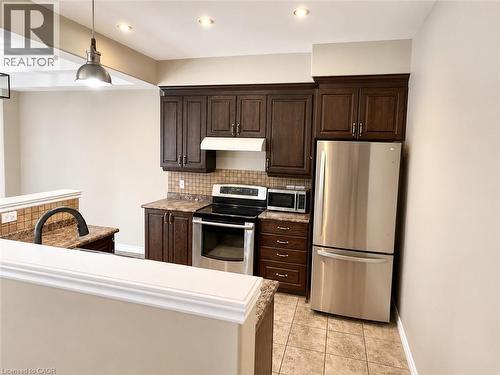 Kitchen featuring dark wood cabinetry, stainless steel appliances, tiled backsplash, and stone-finish countertops - Upper-313 Featherstone Crescent, Kitchener, ON - Indoor Photo Showing Kitchen